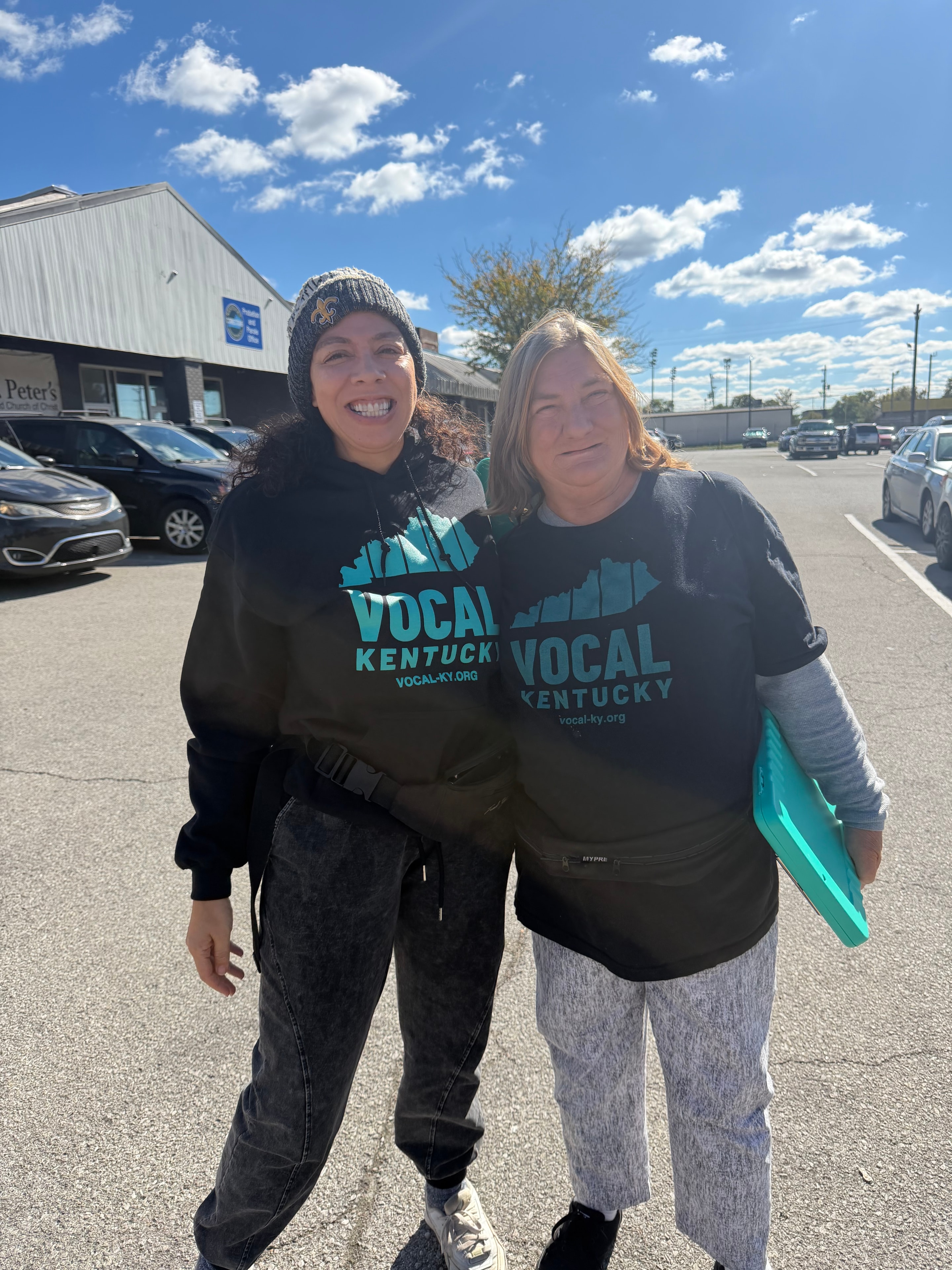 Two people wearing VOCAL Kentucky shirts smiling outside at Operation Warm Hearts