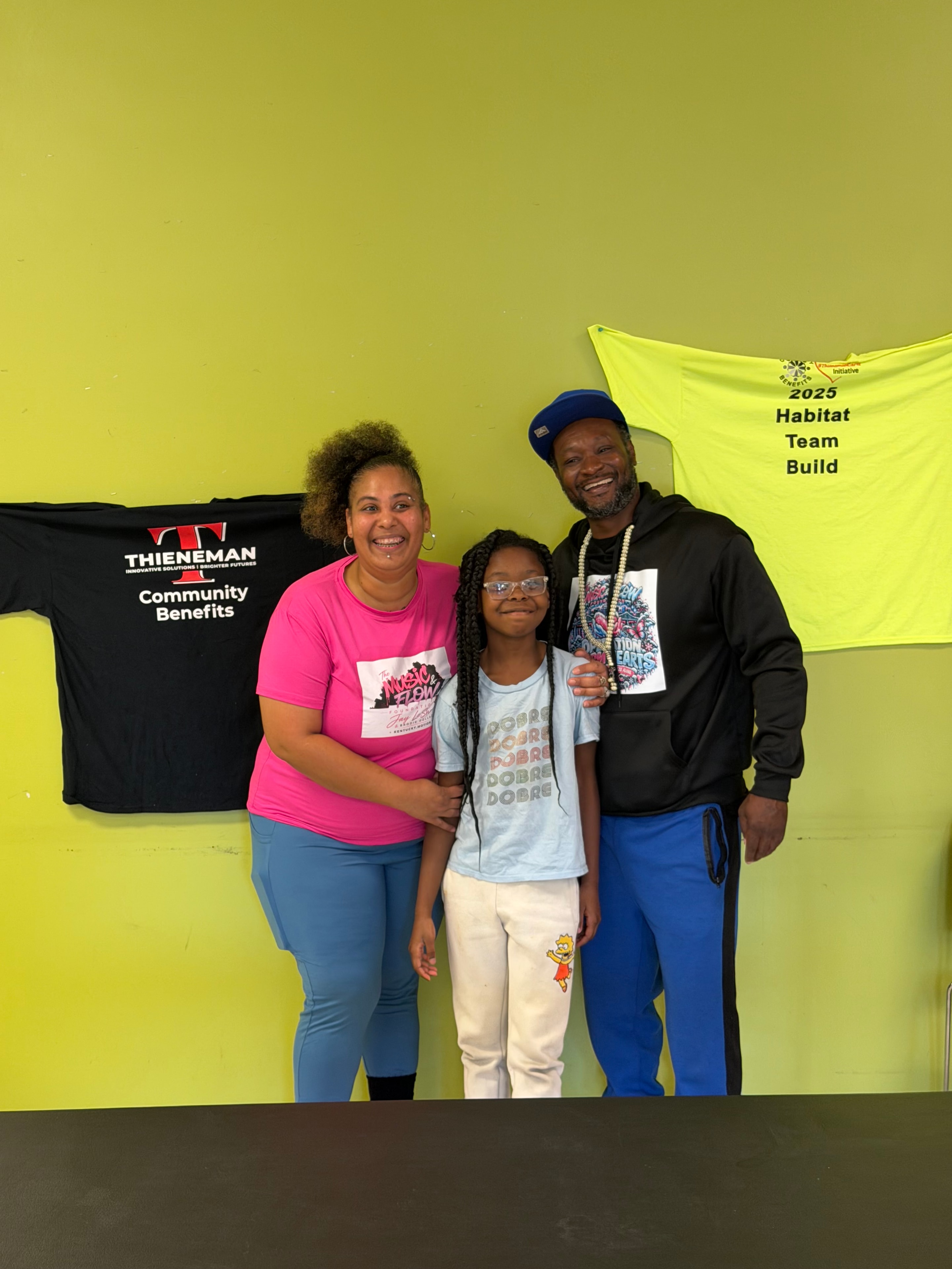 Three people posing together at Operation Warm Hearts with a Thieneman Community Benefits shirt visible